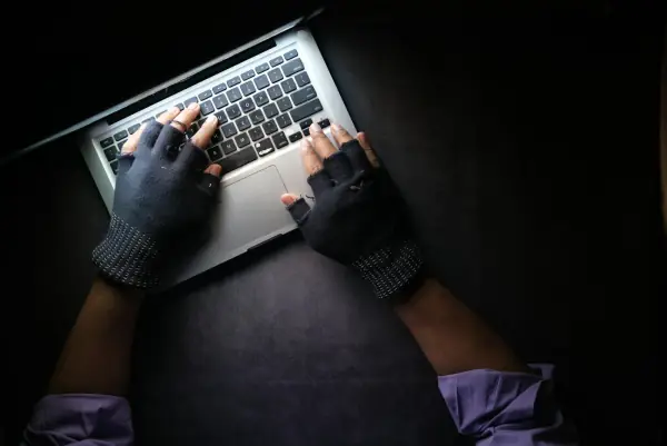 Hands in fingerless gloves typing on a laptop in the dark