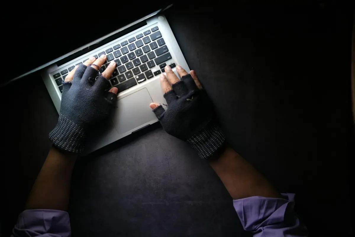 Hands in fingerless gloves typing on a laptop in the dark